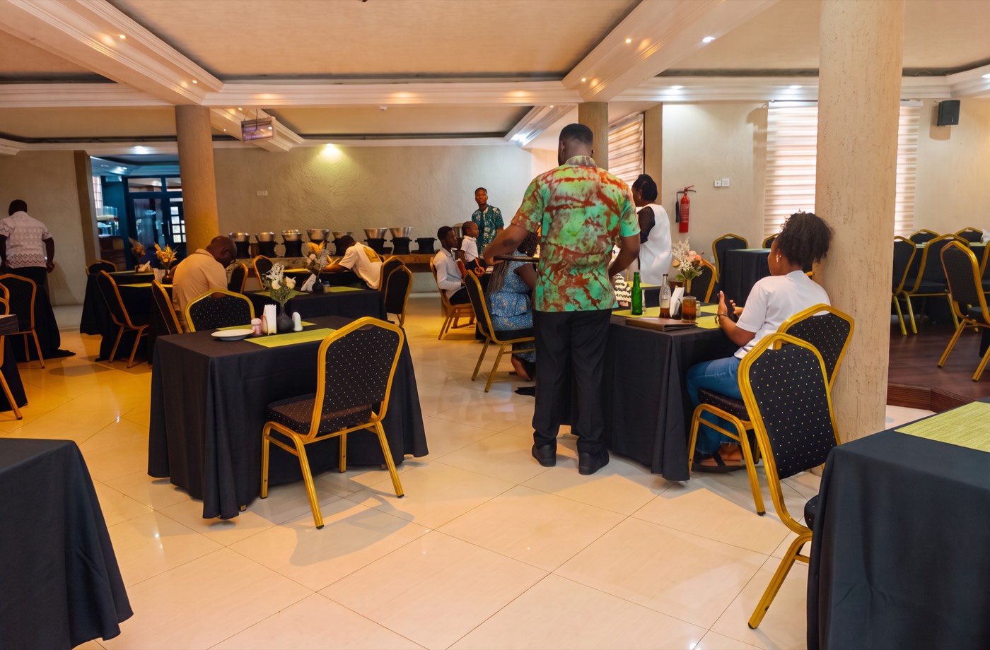 The dining room at Agyeiwaa's Table: guests eating at black-clothed tables with gold banquet chairs, and the buffet counter along the back wall